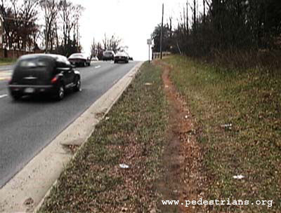 Photo - dirt path worn by pedestrian traffic along a busy road with no sidewalks.
