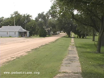 Rural sidewalk by gravel road.