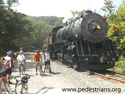 photo - steam engine by bicyclists on trail.